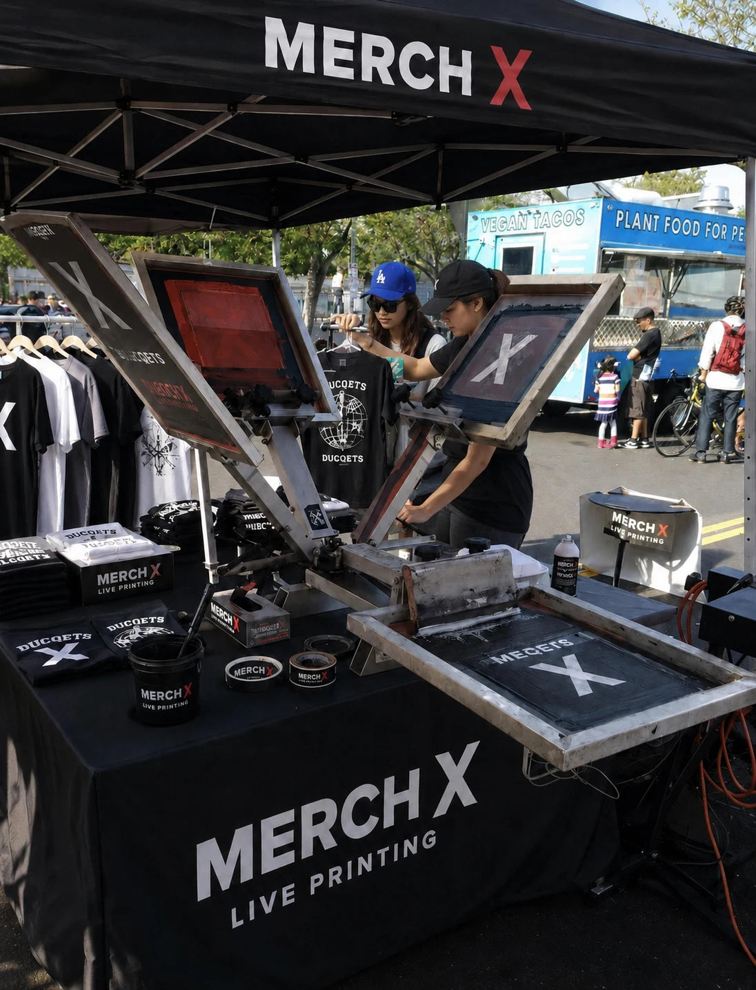 Merch X team printing custom T-shirts under a branded event canopy